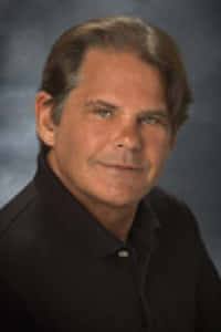 A professional headshot of David Hoines, a real estate expert from Halls Independent Real Estate, wearing a suit and tie, smiling confidently against a neutral gray background