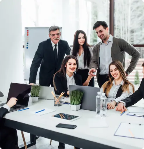 Group of professionals in a meeting room with laptops, papers, and mobile phones on a table.