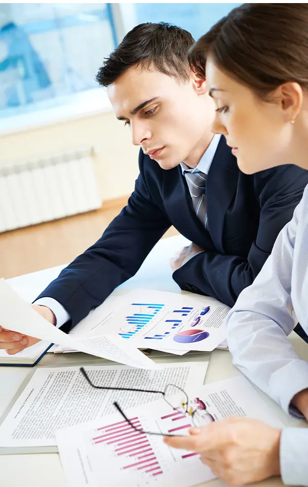 Two professionals examining graphs and reports on a desk.